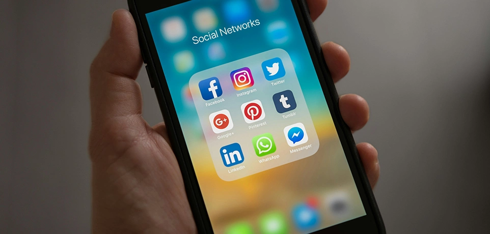 Hand mit Smartphone auf dem Social Media Icons zu sehen sind