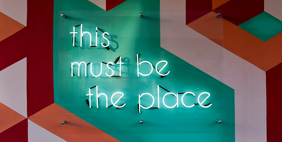Leuchtender Schriftzug an bunter Wand "this must be the place"
