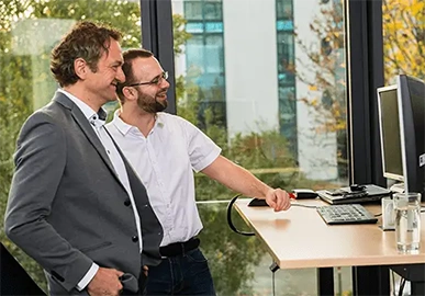 fecher: Ihre Spezialisten hinter der hunter Recruiting Software fecher-Mitarbeiter stehen lachend Steharbeitsplatz Büro